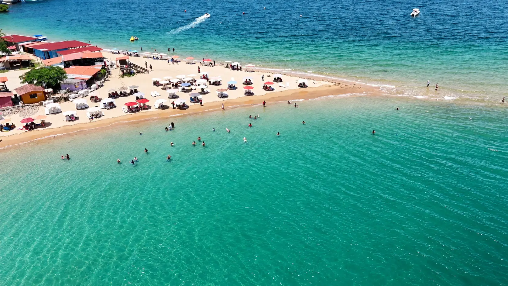Vista aérea de la lengua de arena de Isla Taboga con sombrillas blancas y rojas y aguas turquesas transparentes